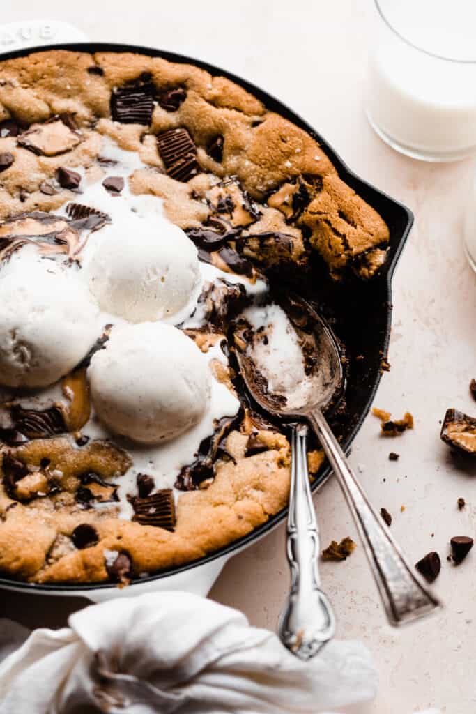 Two spoons in the skillet, with bites of cookie missing, and melty ice cream dripping down from scoops on top.