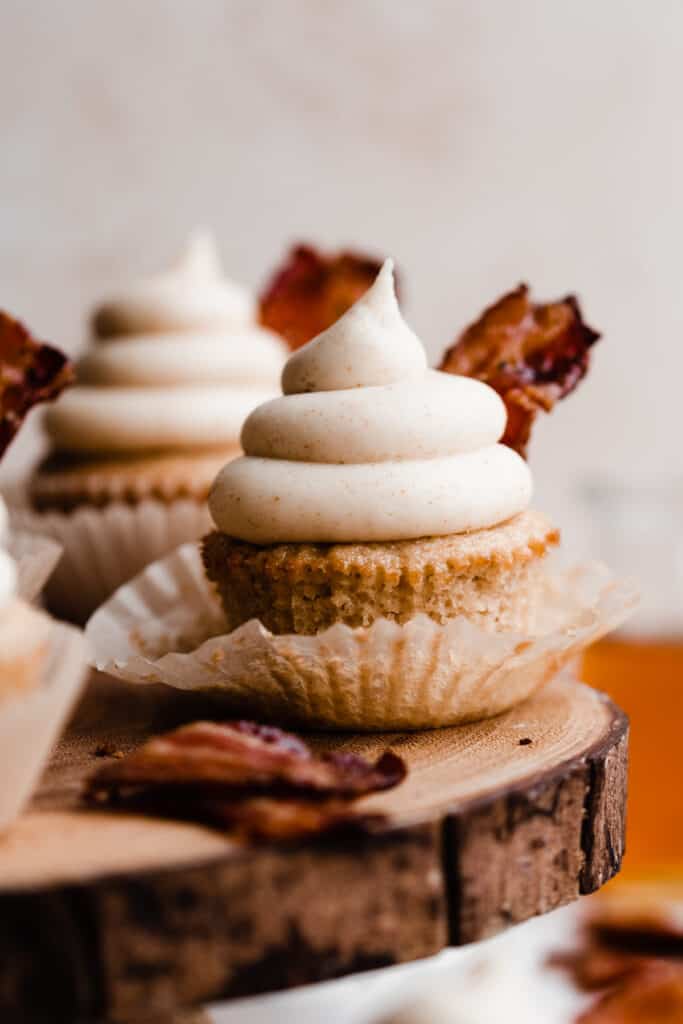 A close-up of a maple bacon cupcake topped with a swirl of frosting and candied bacon.