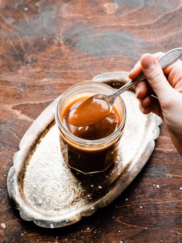 A spoon dipping into a jar of caramel sauce.