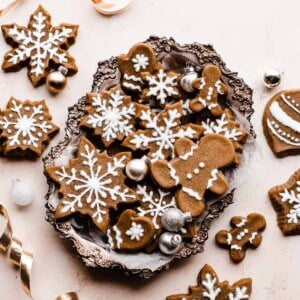 Gingerbread cookies piped with royal icing, in a silver tray surrounded by gold ribbon and mini ornaments.