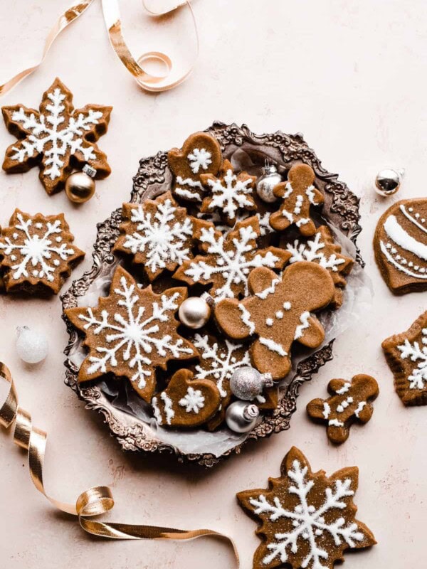Gingerbread cookies piped with royal icing, in a silver tray surrounded by gold ribbon and mini ornaments.