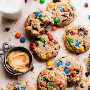 Monster cookies on a light surface, with a bowl of peanut butter and glasses of milk.