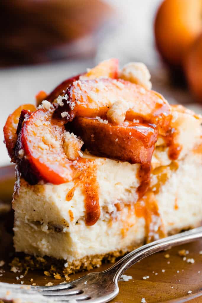 A close-up of a slice of the cheesecake, with juicy peaches on top and peach juice dripping down.