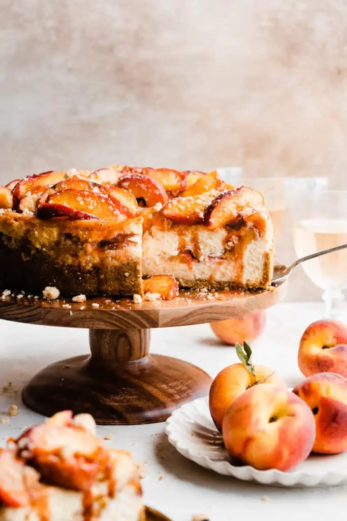 The cheesecake on a cake stand with slices cut, and juicy peaches on top.
