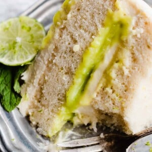 A close-up on a slice of mojito cake with visible lime curd filling, fluffy cake layers, and whipped frosting.