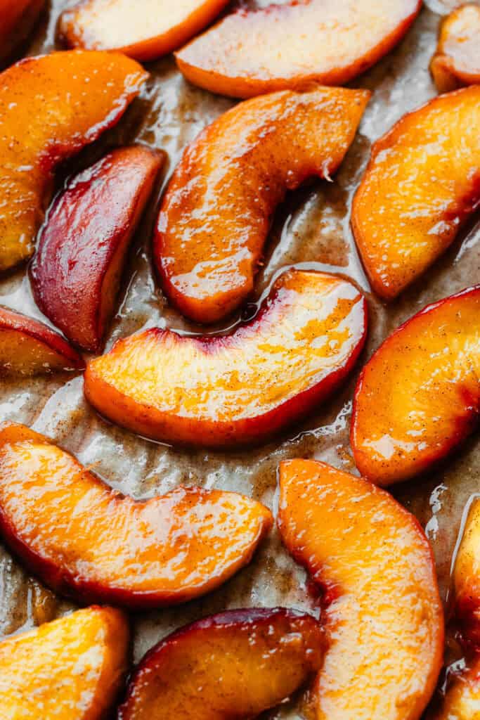 A close-up of juicy roasted peach slices on a baking sheet.