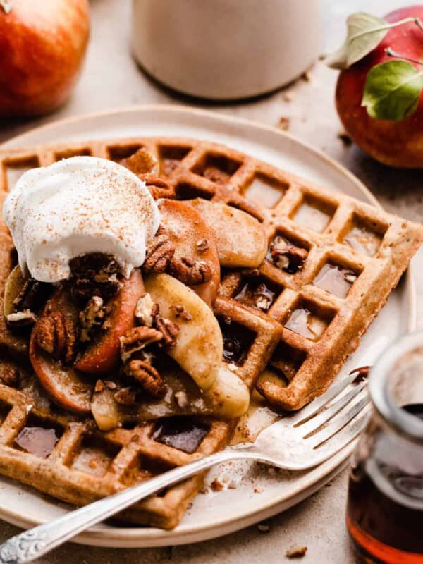 A close-up of the waffles on a plate, topped with the apples and whipped cream.