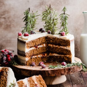 Sliced gingerbread cake on a wooden stand, with sugared cranberries and rosemary trees on top.