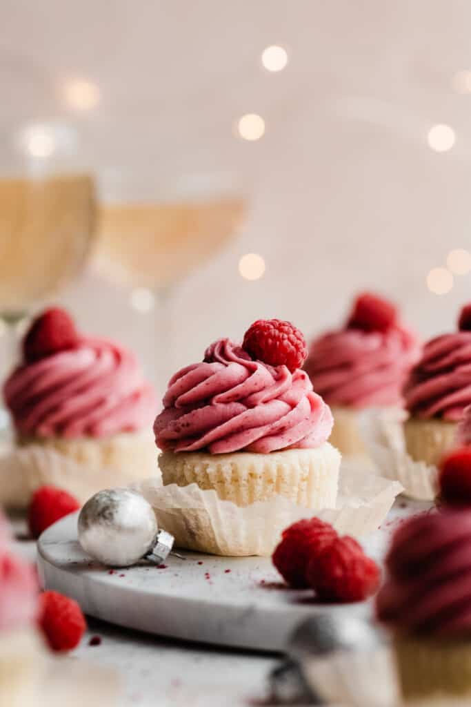 Raspberry frosted cupcakes on a marble surface with twinkling lights.