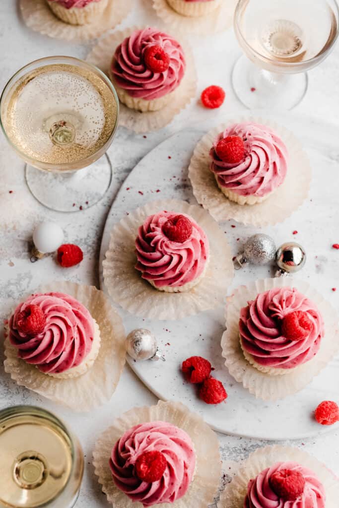 A bird's eye view of the raspberry cupcakes on a marble surface with glasses of champagne.