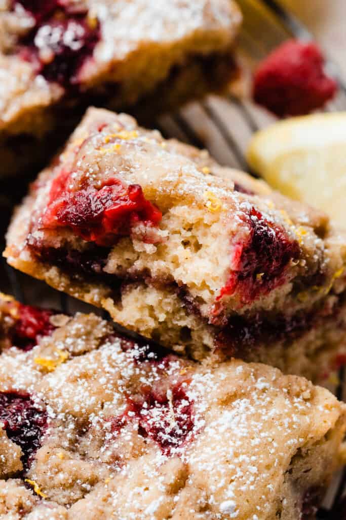 A close-up on a slice of coffee cake with a bite missing, showing the fresh raspberries baked in and the raspberry jam ripple.
