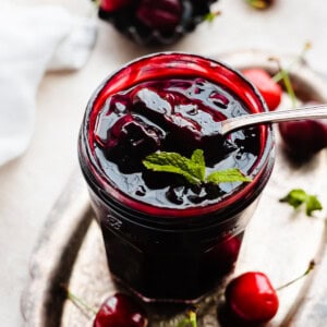 A jar of cherry compote with a spoon going in.