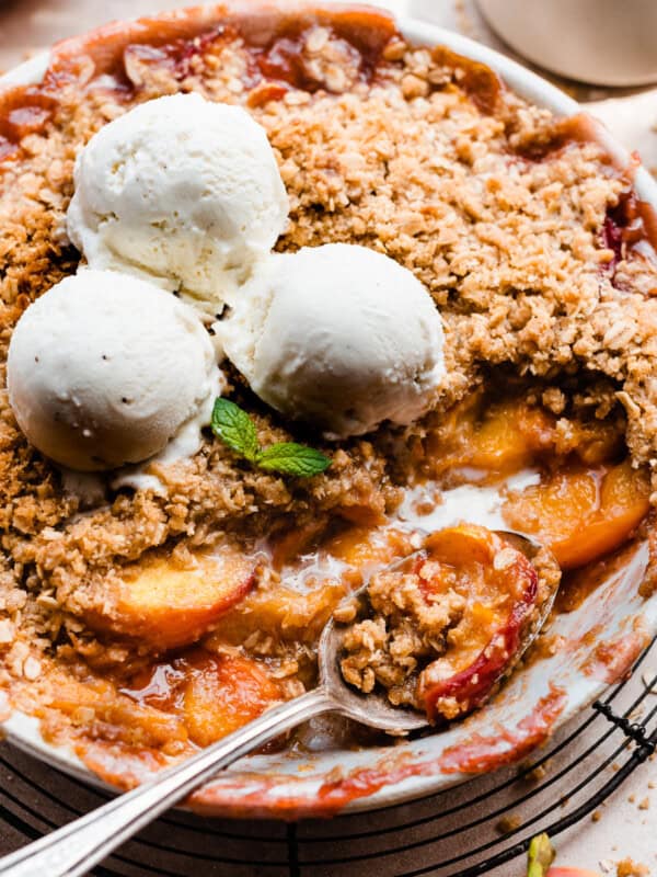 A baking dish of peach crisp topped with scoops of vanilla ice cream.