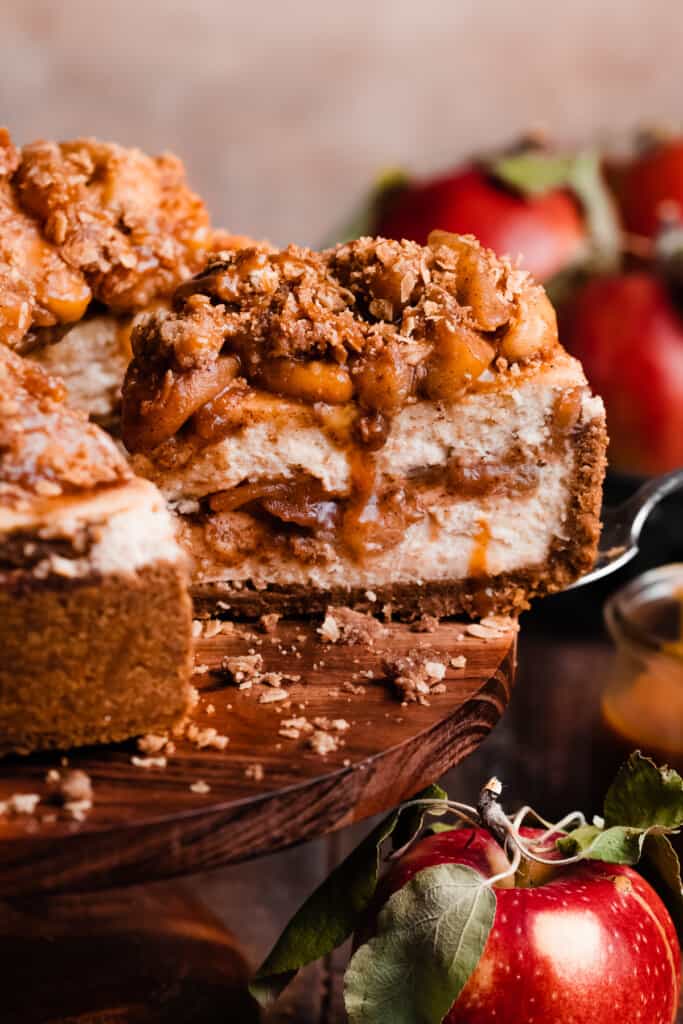 A close-up on a slice of the apple cheesecake being lifted off the cake stand.