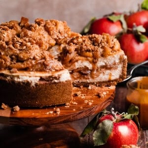 The sliced apple crumble cheesecake on a cake stand, with apple filling, crumble, and caramel on top.