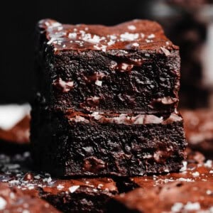 A close-up on a stack of two fudgy brownies topped with flaky sea salt.