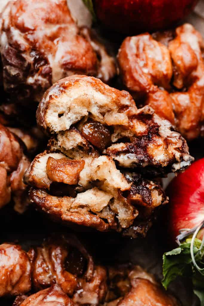 A close-up of two halves of an apple fritter nestled on top of more fritters. The insides are pillowy soft.