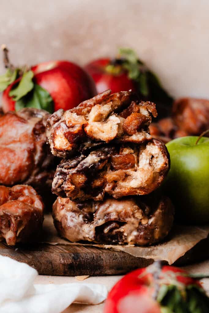 A stack of apple fritter halves with apples in the background.