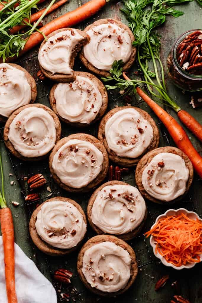 Frosted carrot cake cookies on a green wooden surface.