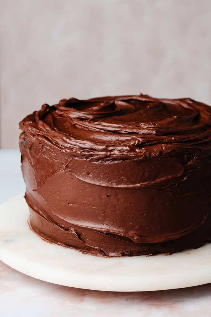 A straight-on look at a cake frosted in shiny, decadent chocolate fudge frosting.