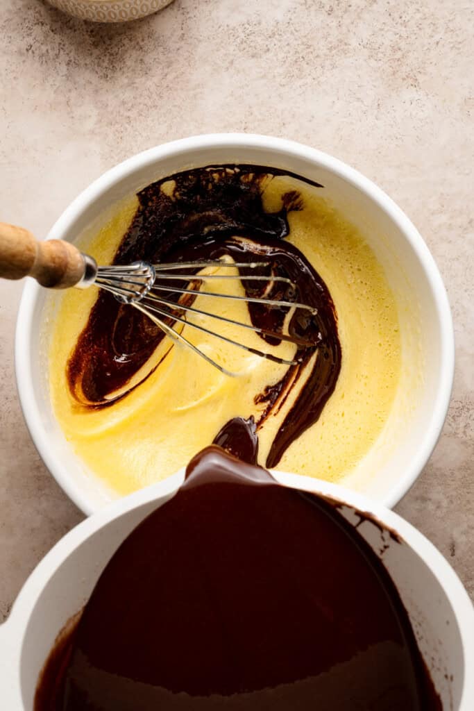 The chocolate mixture being whisked into the egg and sugar mixture.
