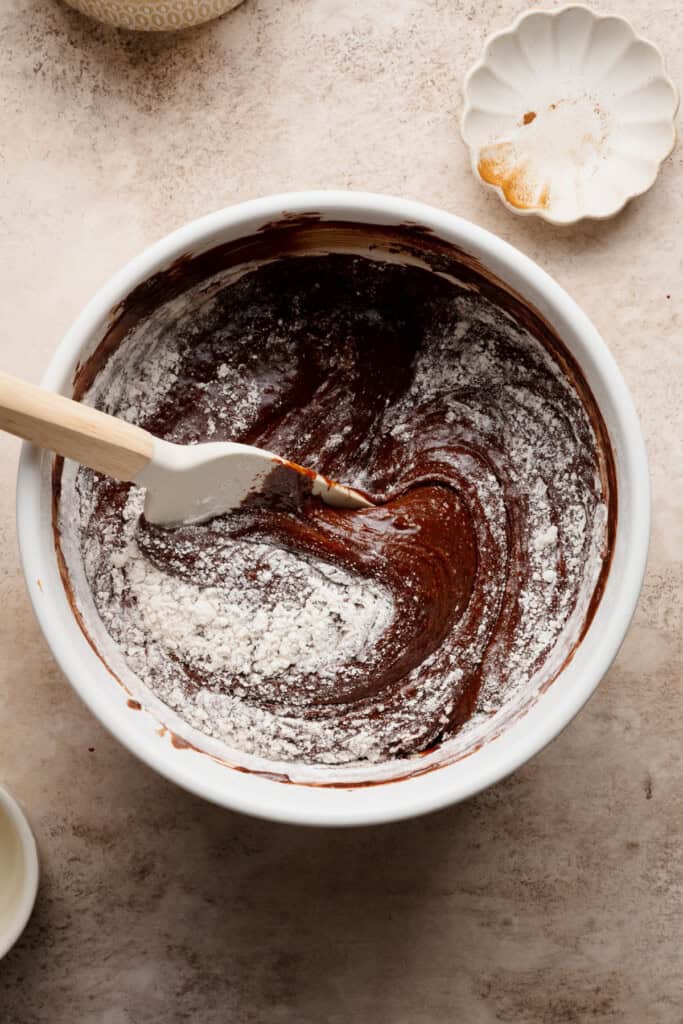 A spatula folding flour into a mixing bowl of the brownie batter.