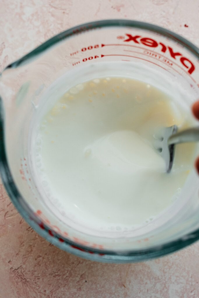 Wet ingredients being whisked together in a glass measuring cup.