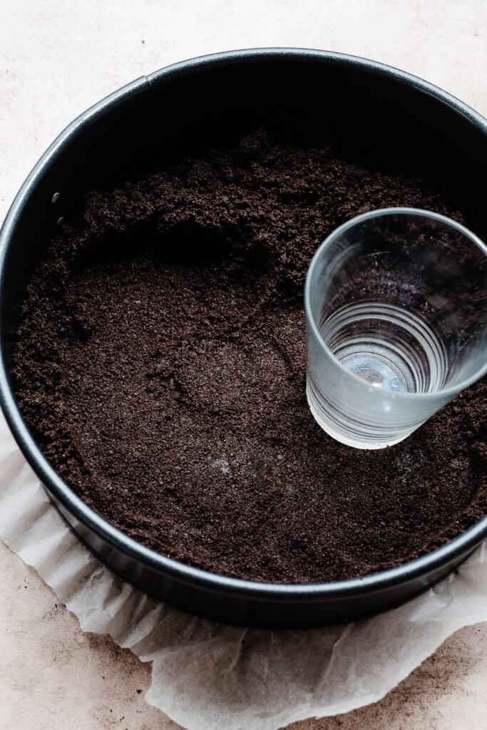 The crust mixture being packed into a springform pan with a juice glass.