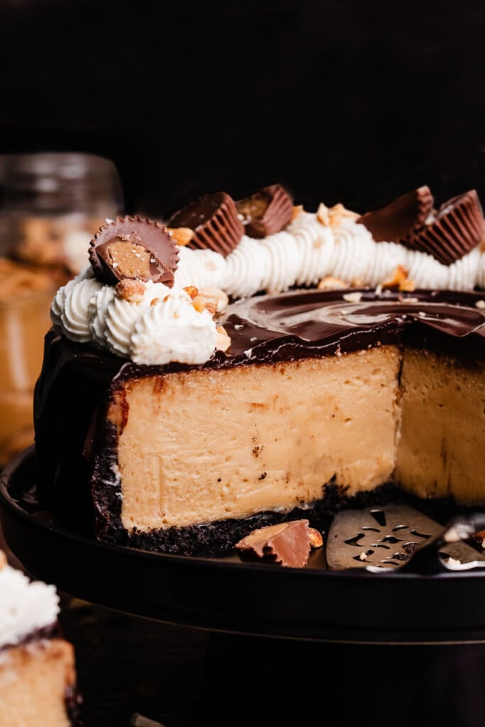 A close-up of a sliced peanut butter cheesecake, topped with ganache and peanut butter whipped cream.