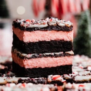 A stack of two peppermint brownies, with visible layers of fudgy brownie, peppermint buttercream, and swirled peppermint bark ganache.