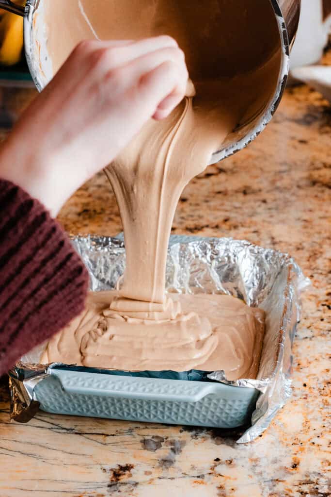 The peanut butter fudge being poured into a foil lined pan.