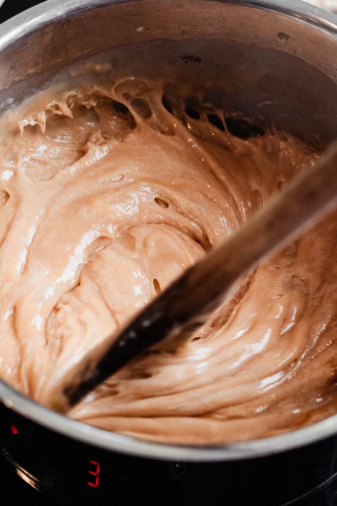 A spoon stirring the toffee mixture as it cooks in a pot on the stovetop.