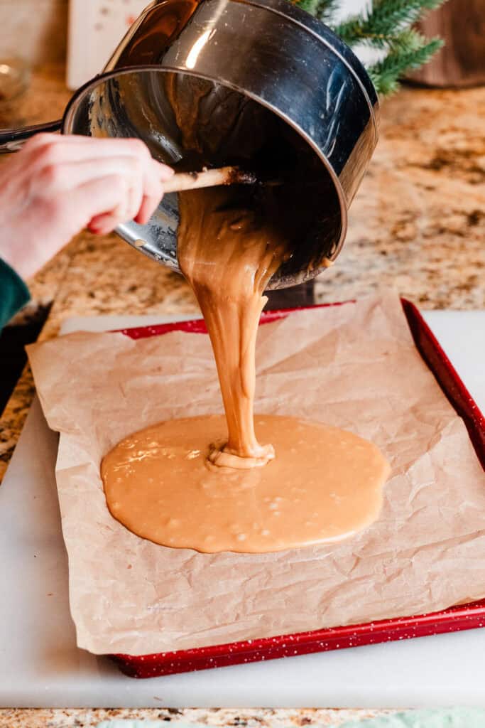 Toffee mixture being poured onto a lined cookie sheet.