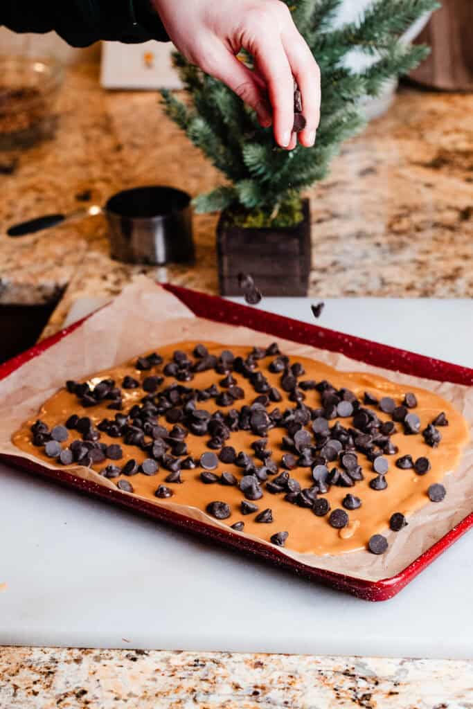 My hand sprinkling chocolate chips over the warm toffee mixture on a cookie sheet.