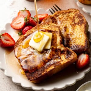 Slices of golden brown brioche french toast on a plate, with butter and maple syrup.