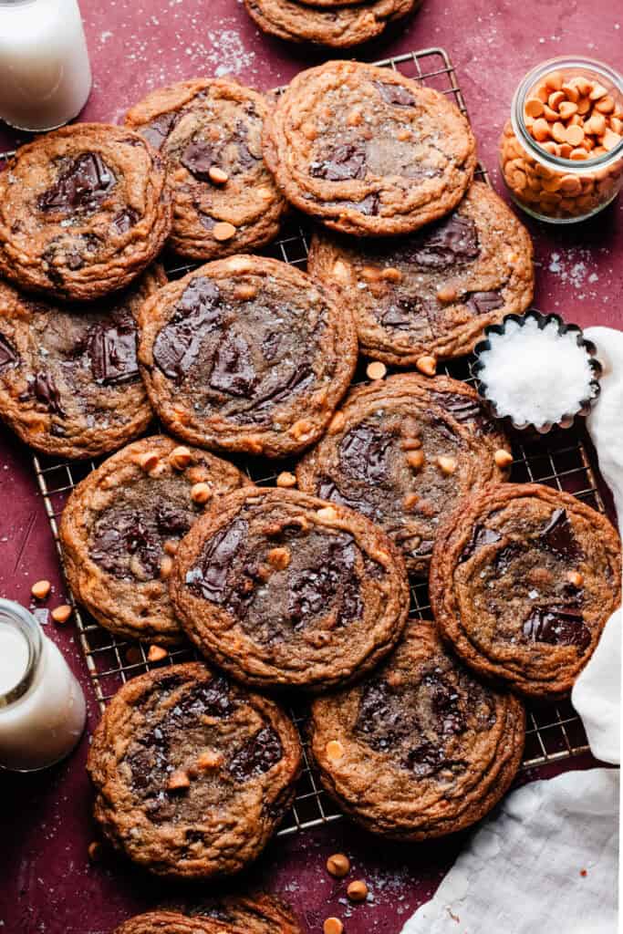 Thin and chewy butterscotch chocolate chip cookies on a wire rack, on a burgundy background.