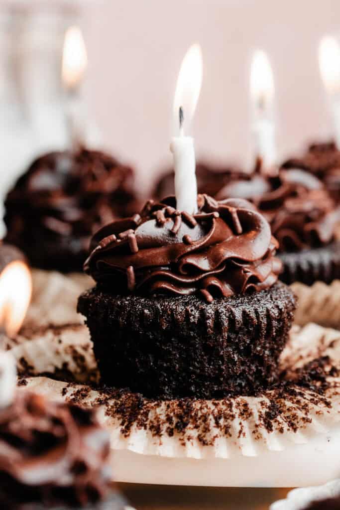 A close-up on a chocolate frosted chocolate cupcake, with a lit birthday candle stuck in it.