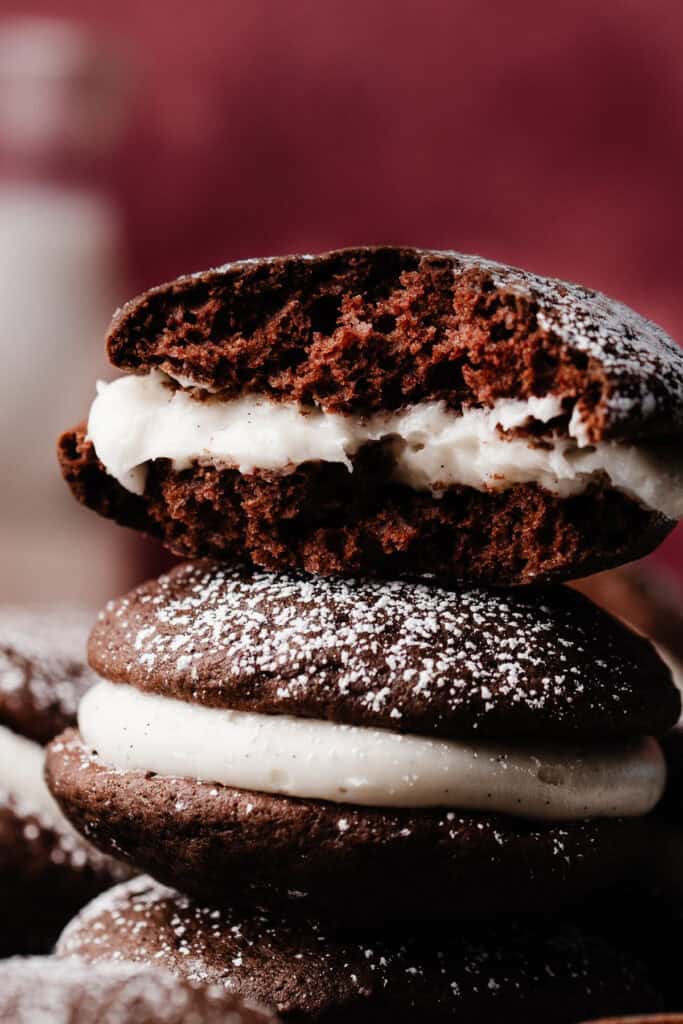 A stack of chocolate whoopie pies, with half of the top one broken off, to show the fluffy texture inside.