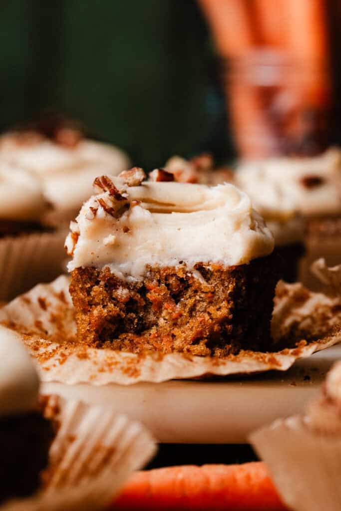 A close-up of a carrot cake cupcake with a bite missing, showing the moist texture inside.
