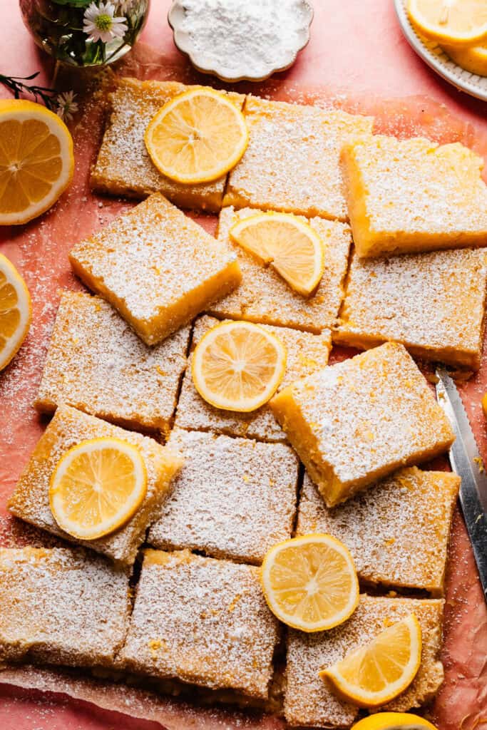 The sliced lemon bars on a pink surface, dusted with powdered sugar.