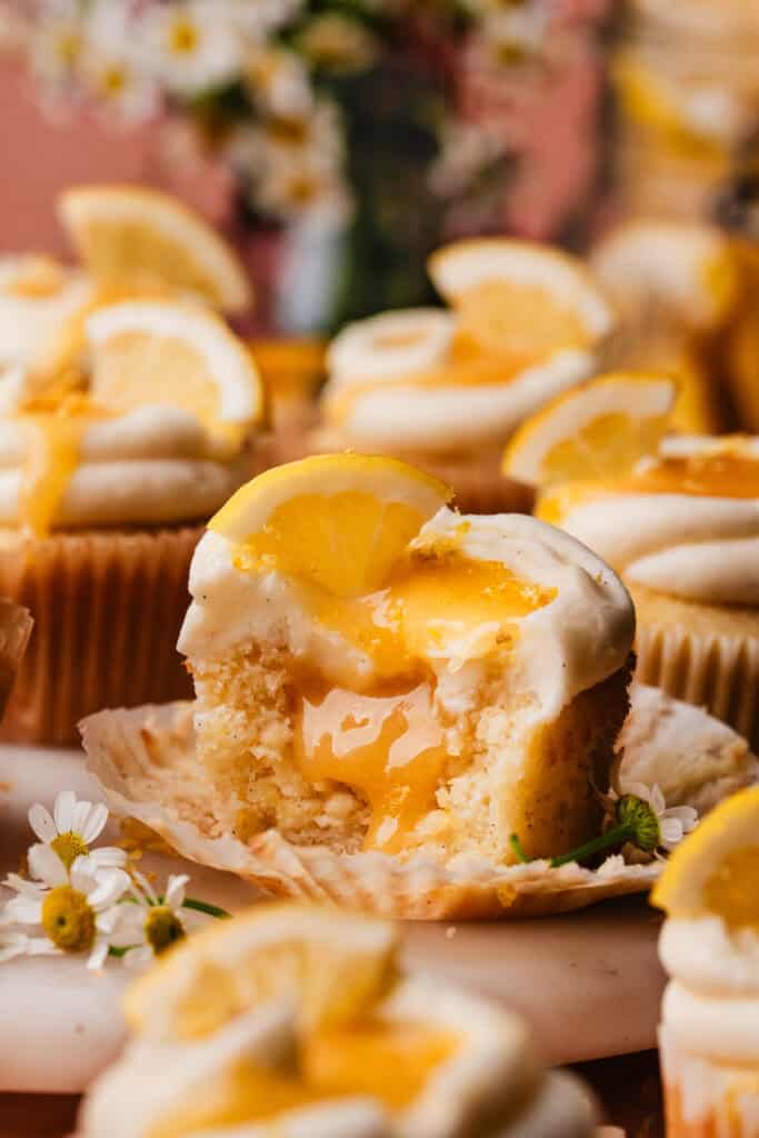 A lemon cupcake with bites missing - showing the lemon curd filling inside.