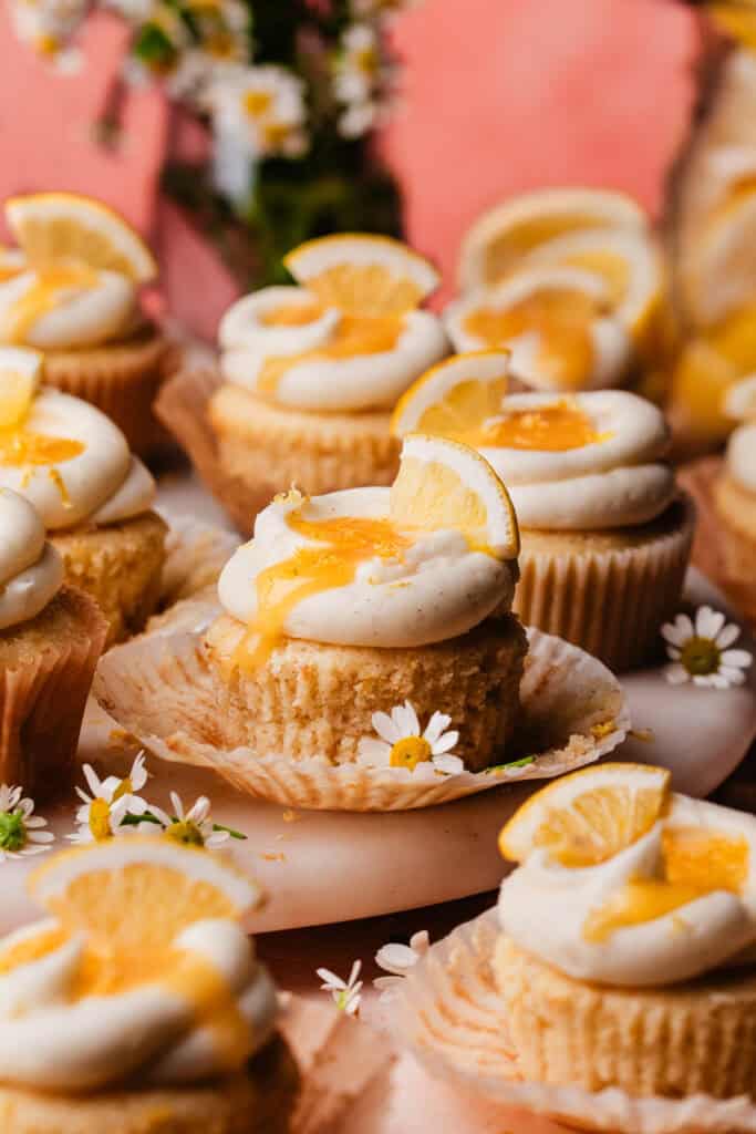 Lemon Cupcakes on a marble cake plate, with small flowers and lemon slices scattered around.