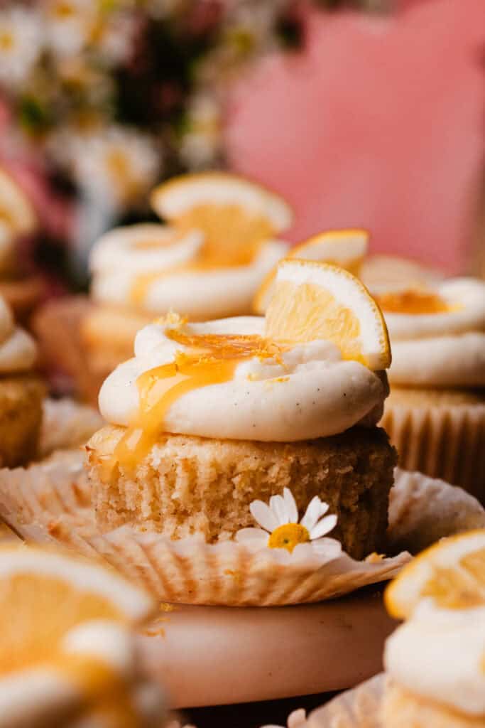 A close-up on a lemon cupcake. It's topped with swirls of lemon cream cheese frosting, lemon curd, and a small lemon slice.