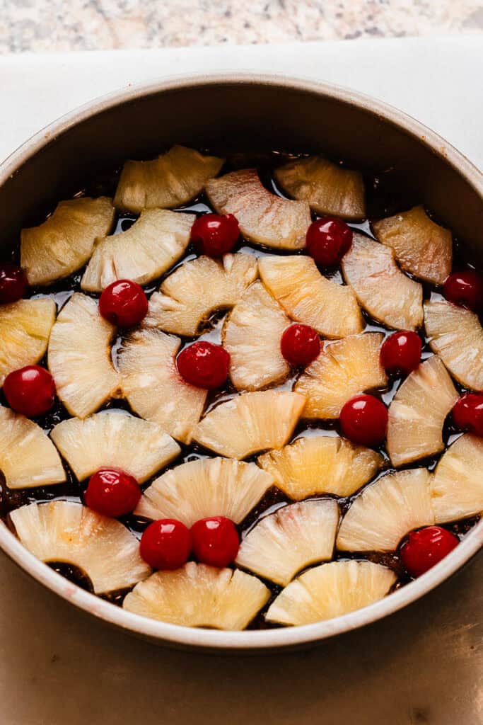 Pineapple slices and maraschino cherries layered in the cake pan, over the brown sugar and butter.