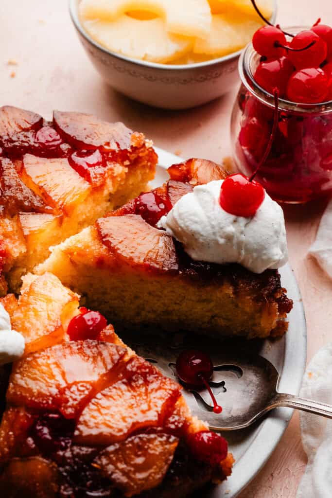 Slices of the pineapple upside down cake on a cake plate, topped with whipped cream and maraschino cherries.