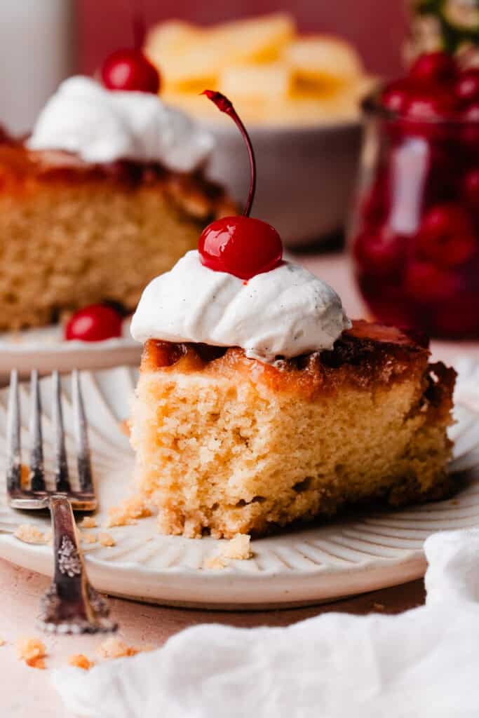 A slice of pineapple upside down cake on a plate, with a bite missing to show the fluffy texture inside.
