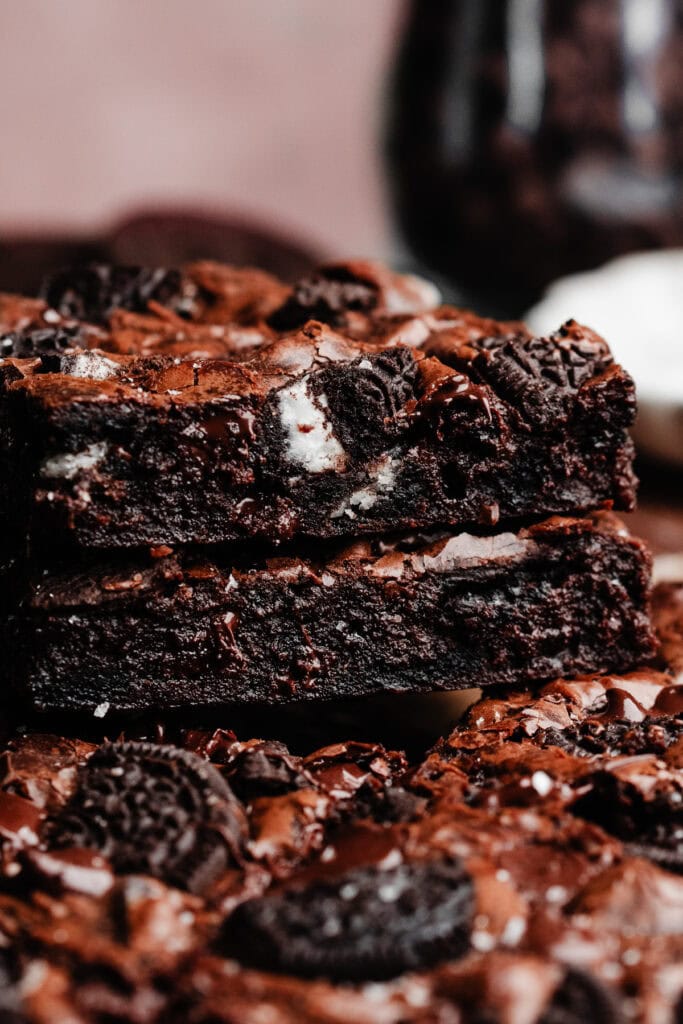 A stack of two oreo brownies, with a jar of oreo pieces in the background.