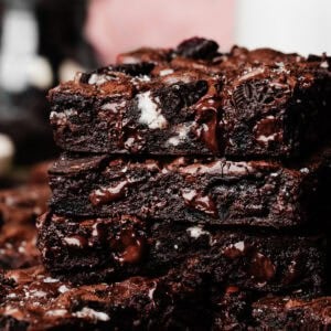 A stack of three fudgy oreo brownies, with a jar of oreo pieces and a bottle of milk visible in the background.