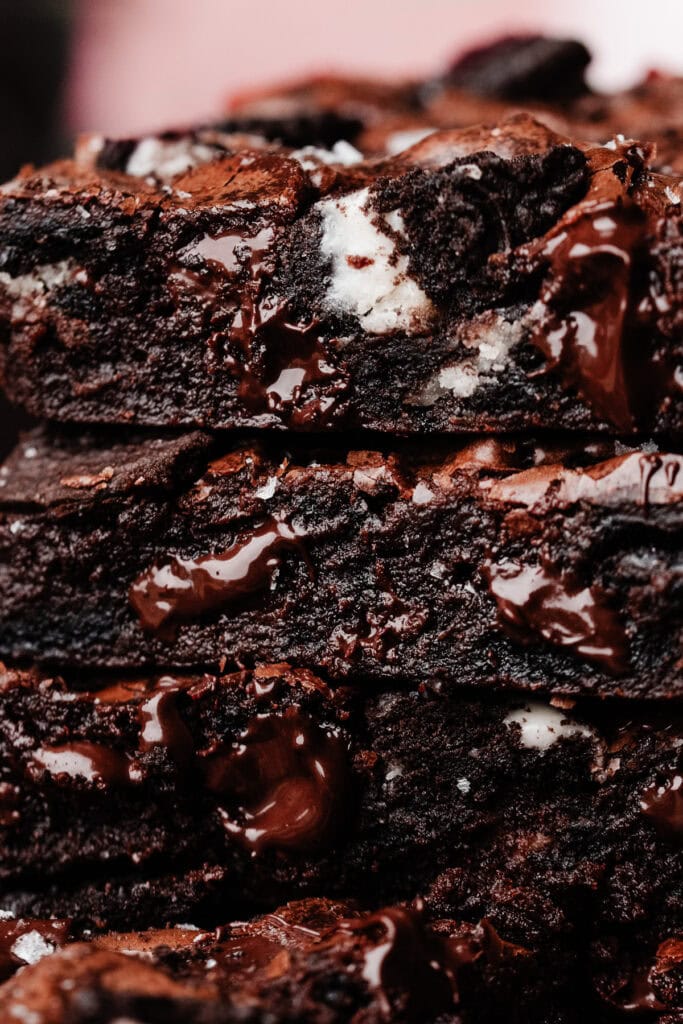 A close-up on a stack of three fudgy oreo brownies, giving you a very close look at the fudgy texture of the brownies, the oreo pieces inside, and the melty chocolate chips.