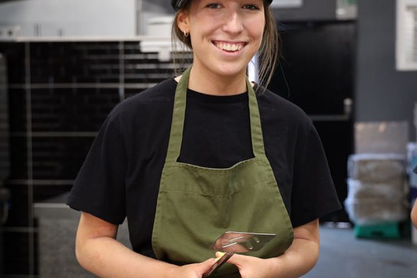 Dundee woman smiling in a kitchen wearing a black cap and green apron at BlueCoo Creative.
